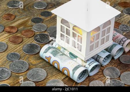 Casa in cima alle banconote in dollari americani arrotolati in tubo e molti noi monete. Cassa domestica e risparmio di beni finanziari per investimenti immobiliari Foto Stock