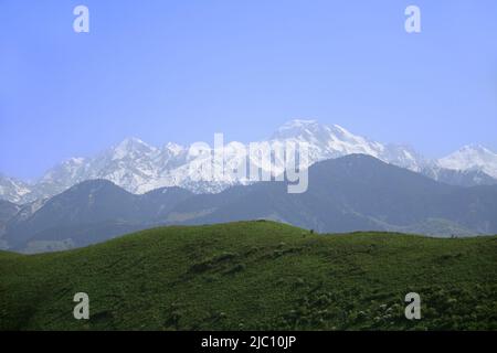 Enorme cresta innevata alpina con picco Talgar con catene montuose e verdi colline ai piedi in estate, soleggiato Foto Stock