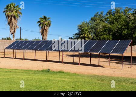 Grande quantità di pannelli solari in un'area sabbiosa semi arida. I pannelli sono montati su un telaio metallico. Sullo sfondo si trovano palme. Foto Stock