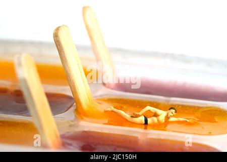 Fotografia di personaggi giocattolo in miniatura. Concetto creativo di vacanza in piscina estiva. Un uomo che fa il nuoto libero stile sul bastone del gelato della gelatina del budino. Imag Foto Stock