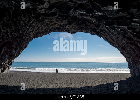 Donna in piedi in una grotta di roccia basaltica sulla spiaggia di Reynisfjara in Islanda Foto Stock