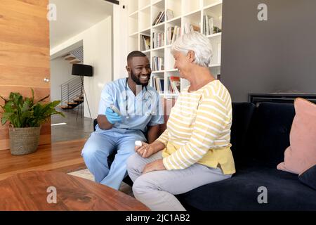 Operatore sanitario africano americano maschile che misura lo zucchero nel sangue della donna anziana caucasica utilizzando glucometro Foto Stock