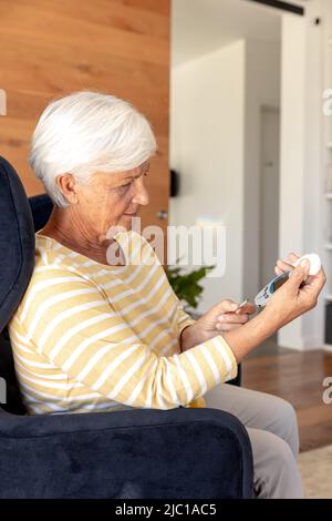 Donna anziana caucasica che misura il suo zucchero nel sangue usando glucometro a casa Foto Stock