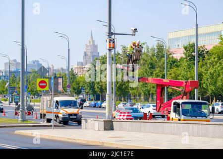 Mosca. Russia. Giugno 9, 2022. Gli ingegneri elettronici in un carrello di una torre mobile riparano una telecamera di sicurezza su un palo su una strada a Mosca. Messa a fuoco selettiva. Foto Stock