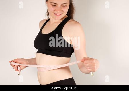 Una donna misura la circonferenza dell'addome con un nastro di centimetri, primo piano. Concetto di dimagrimento Foto Stock