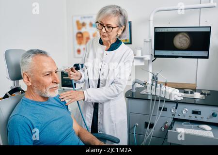 Endoscopia auricolare. ENT medico che esamina l'orecchio dell'uomo maturo usando l'endoscopio alla clinica otolaringologica Foto Stock