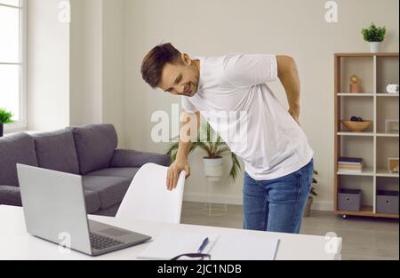 Il giovane uomo si stanca e sente un intenso mal di schiena dopo aver lavorato alla scrivania del computer Foto Stock