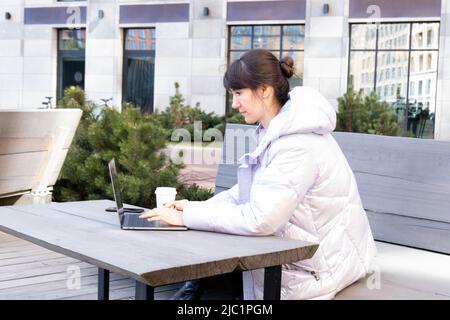 Happy casual bella donna che lavora in un computer portatile seduto in un bar terrazza all'aperto. La ragazza guarda il notebook. Spazio di copia. Foto Stock