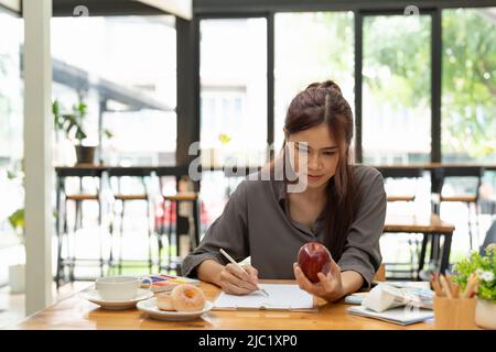 Giovane grafica femminile asiatica che disegna mela sul suo progetto con un moderno luogo di lavoro creativo Foto Stock