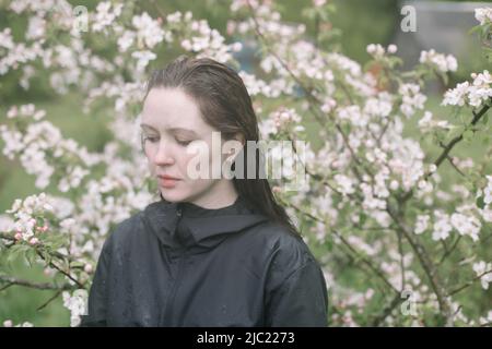 ritratto emozionale di una giovane donna in piedi sola sotto la pioggia all'aperto in primavera. Foto Stock