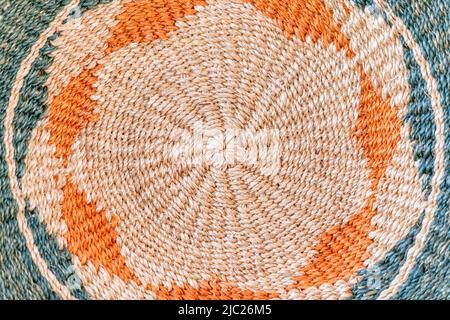 Fibre di iuta arrotolate formano un motivo circolare a tappeto in crema, arancione e blu-verde spento, creando uno sfondo tessile intrecciato dettagliato. Foto Stock