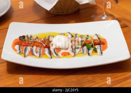 Filetti di acciuga (salati di fresco) in olio d'oliva e tartare di pomodoro fresco con una paletta di formaggio cremoso Foto Stock