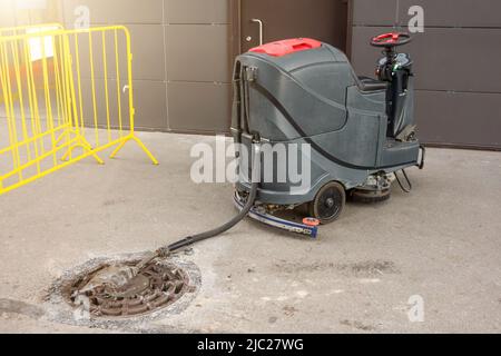 Servizi di pulizia e cura del pavimento con lavatrice professionale all'esterno dell'edificio, l'acqua sporca viene drenata Foto Stock