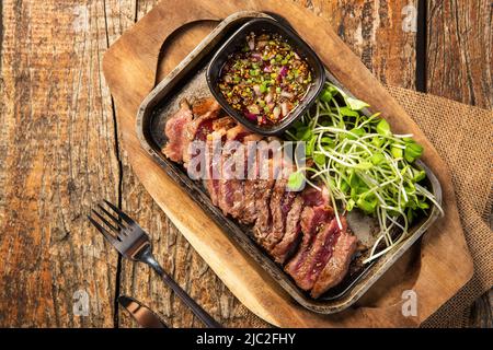 Bistecca di controfiletto su una padella calda su un piatto di legno con salsa da immersione decorata con germogli di girasole, World food day Foto Stock