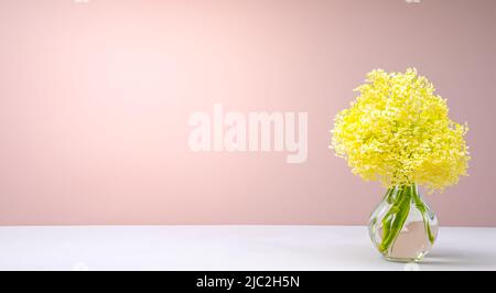 Bouquet di piccoli fiori gialli in vaso di vetro sul tavolo su sfondo rosa Foto Stock
