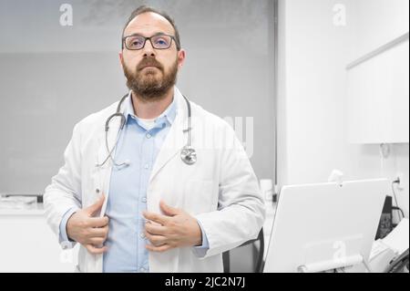 Medico uomo di mezza età che indossa il cappotto medico bianco alla clinica con espressione seria. Foto di alta qualità Foto Stock