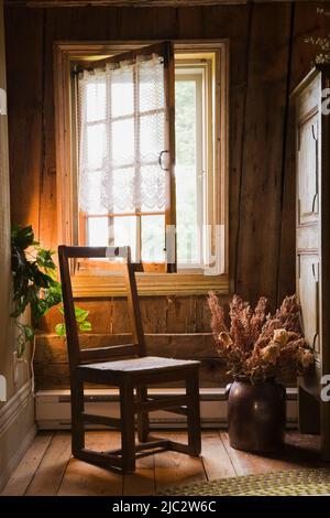 Vecchia sedia di legno accanto alla finestra nella camera da letto degli ospiti al piano superiore all'interno della vecchia casa in stile cottage del regime francese del 1752. Foto Stock