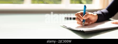 Close-up di una imprenditrice la mano riempiendo il modulo di appalto Foto Stock