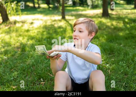 un bambino nel parco tiene le fatture del dollaro davanti lui e le getta davanti lui Foto Stock