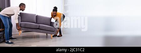 Vista laterale di un sorridente giovane africana matura il sollevamento divano nel soggiorno Foto Stock