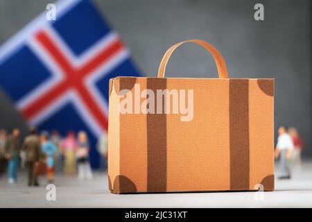 Valigia di cartone, giocattolo di plastica e una bandiera su sfondo astratto, un concetto sul tema del trasferimento o dell'immigrazione in Islanda Foto Stock
