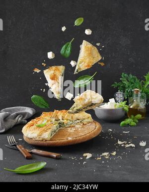 Cucina greca tradizionale. Torta di Spanakopita e pezzi con spinaci e formaggio feta su sfondo scuro. Cibo di Lavitazione Foto Stock