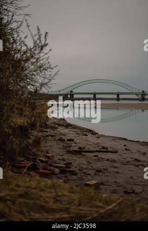 Naufragio sulla spiaggia sabbiosa, Wigg Island, con il Runcorn Bridge / Silver Jubilee Bridge sullo sfondo- Runcorn, Regno Unito. Foto Stock