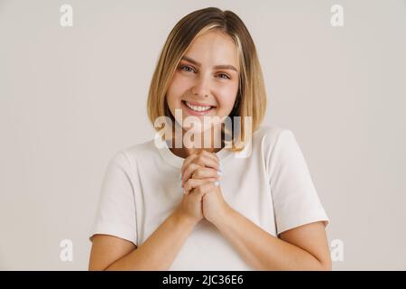 Giovane donna bionda sorridente mentre tiene le mani insieme isolato su sfondo bianco Foto Stock