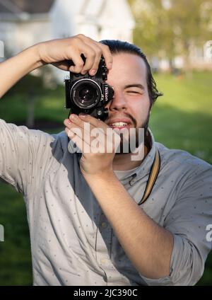 Un giovane maschio adulto bearded con la macchina fotografica ha puntato al visore che fa una foto ad un parco in primavera o estate, Lancaster, Pennsylvania Foto Stock
