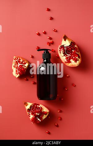 Pompate il flacone marrone con lo shampoo estratto di melograno su sfondo rosso. Disposizione piatta, vista dall'alto. Foto Stock