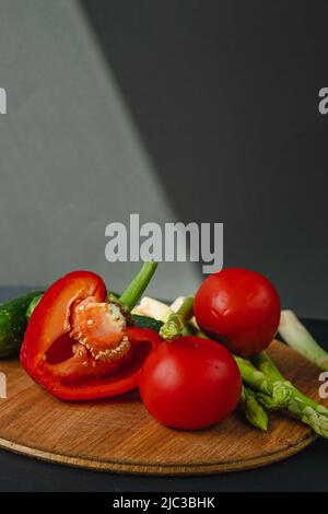 rami di asparagi verdi freschi, peperoni, pomodori e cetrioli su un asse di legno, sfondo grigio scuro, vista dall'alto. Concetto di trend di base con copia sp Foto Stock