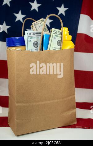 Un sacchetto di carta marrone semplice riempito di generi alimentari e soldi su una bandiera americana Foto Stock
