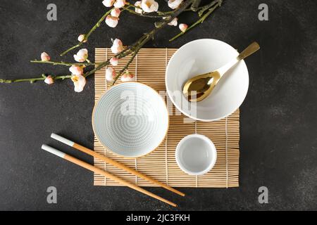 Ciotole cinesi con bacchette e bel ramo su sfondo nero Foto Stock