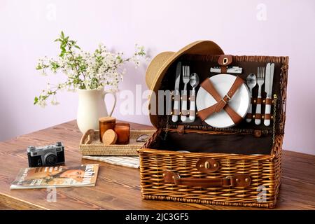 Cestino con stoviglie, macchina fotografica, rivista e rami fioriti in vaso  sul tavolo vicino alla parete della luce Foto stock - Alamy