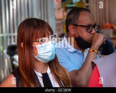 Medellin, Antioquia, Colombia - Febbraio 19 2022: Una donna colombiana con capelli lunghi rossi indossa occhiali bianchi e una maschera ciano sulla strada vicino ad altre PE Foto Stock