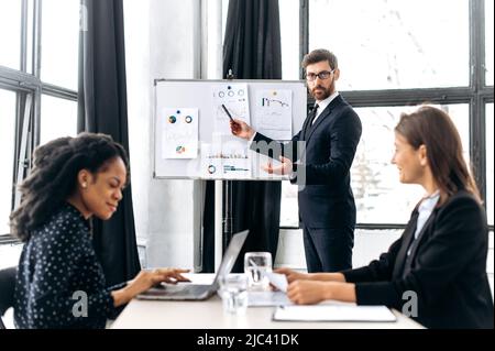 Lavoro di squadra, collaborazione. Influente amministratore delegato caucasico attraente maschile, tenendo gruppo brainstorm, discutendo idee per un nuovo progetto di business, fa una presentazione business plan per le sue partner femminili Foto Stock