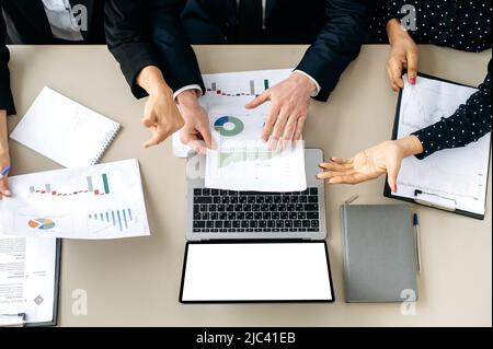 Collaborazione aziendale. Vista dall'alto della scrivania dell'ufficio con le mani delle persone, grafici finanziari, laptop aperto con uno schermo bianco bianco bianco bianco bianco mock-up, spazio vuoto per la presentazione Foto Stock