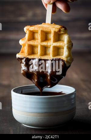 Una cialda viene immersa nel cioccolato fuso e gocciola in una ciotola. Foto Stock