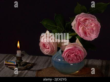 Inglese rosa in vaso su un tavolo e una candela bruciante con sfondo scuro Foto Stock