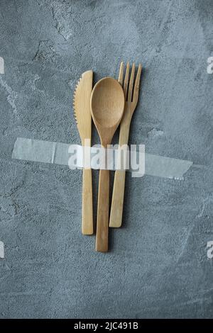 Foto di eco concetto di arredamento domestico biologico, coltello, cucchiaio e forcella incollando con nastro adesivo su parete grigia in gesso spalmato. Produzione senza sprechi di Foto Stock