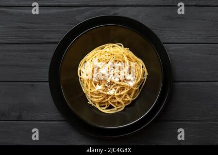 Cacio e Pepe - Pasta Italiana con formaggio e pepe sul piatto nero su sfondo scuro. Vista dall'alto, disposizione piatta Foto Stock