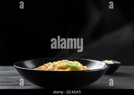 Cacio e Pepe - Pasta Italiana con formaggio e pepe sul piatto nero su sfondo scuro Foto Stock