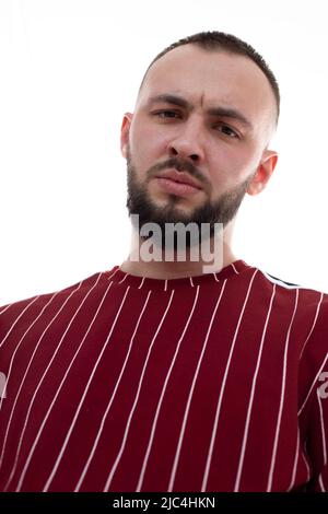 Primo piano immagine verticale del volto dell'uomo non rasato che guarda la fotocamera in uniforme rossa. Vista dell'angolo basso dell'Hipster Foto Stock