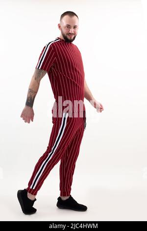 Brunet tatuò bell'uomo in posa, passeggiando in studio, guardando la fotocamera. Sportivo e atleta maschio Foto Stock