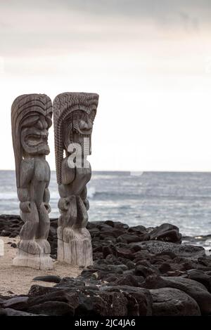 Figura guardiana in legno, tiki di fronte al muro di pietre laviche e l'Oceano Pacifico, Puuhonua o Honaunau National Historical Park, Big Island, Hawaii Foto Stock