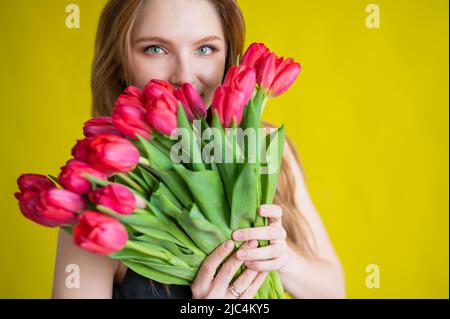 Donna con un bouquet di tulipani rossi su sfondo giallo. La ragazza felice in un vestito nero tiene un'armatura di fiori . Regalo per San Valentino. La maggior parte Foto Stock