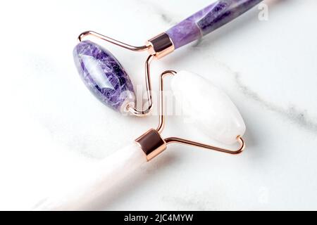 Primo piano dei rulli di quarzo Massage per il viso di nefrite naturale rosa e ametista. Strumenti di massaggio Gua Sha. Anti età e sollevamento a casa. Cura della pelle Foto Stock