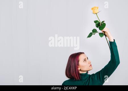 Donna con un fiore di rosa giallo in mano su sfondo chiaro. Foto Stock