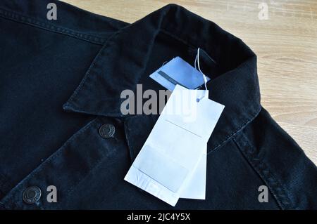 Giacca in denim jeans nero e carta tag vendita bianca, su pavimento in legno Foto Stock