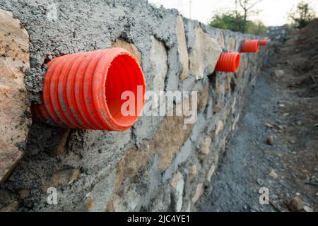 Una fila di colverti arancioni o tubi di uscita dell'acqua attraverso un muro di contenimento di pietra per il drenaggio delle tempeste nelle colline di Uttarakhand India. Foto Stock